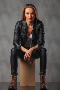 rocker in black leather jacket posing seated in studio background looking at the camera and resting
