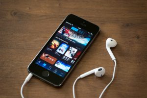Kiev, Ukraine - June 5, 2014: Brand new Apple iPhone 5S with iTunes store application on the screen lying on a desk with headphones. iTunes is the media library with player for download and organize media files, developed by Apple Inc.